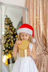 Little cute girl in Santa hat opens a Christmas present.