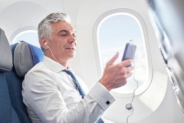 Businessman listening to music with headphones mp3 player on airplane