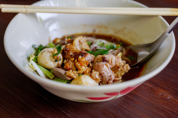 Close up view of Spicy Thai Boat rice Noodle Soup,  Kuai Tiao Ruea, serve on ceramic bowl on wooden table. 