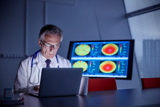 Focused male surgeon working at laptop in hospital