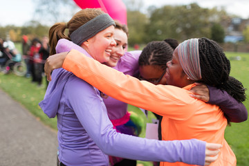 Happy female runners hugging at charity run finish line, celebrating