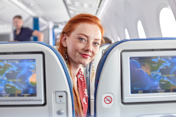 Portrait smiling young woman with red hair and freckles on airplane