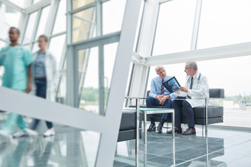 Male surgeon with x-ray talking to patient in hospital lobby