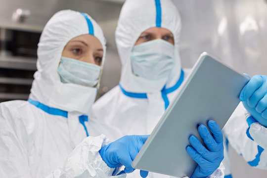 Scientists in protective clean suits using digital tablet