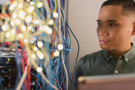 Focused male IT technician examining wires on server panel