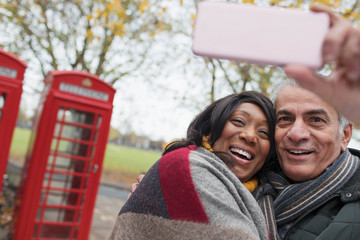 Affectionate senior couple taking selfie in autumn park in front of red telephone book