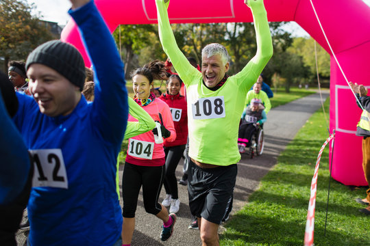 Enthusiastic runners cheering, crossing charity run finish line