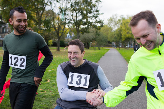 Smiling male runner shaking hands friend in wheelchair at charity race in park