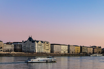 Obraz premium Tourist cruise boat traveling up the Danube river after sunset.