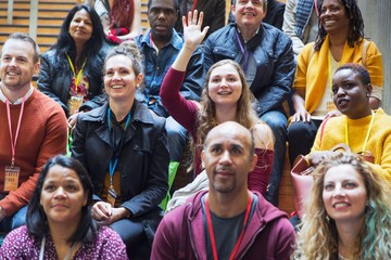 Woman participating, raising hand in conference audience