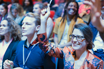 Smiling woman in conference audience raising hand