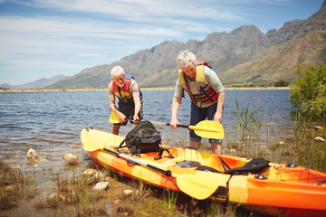 Active senior couple preparing kayak at sunny, summer lake