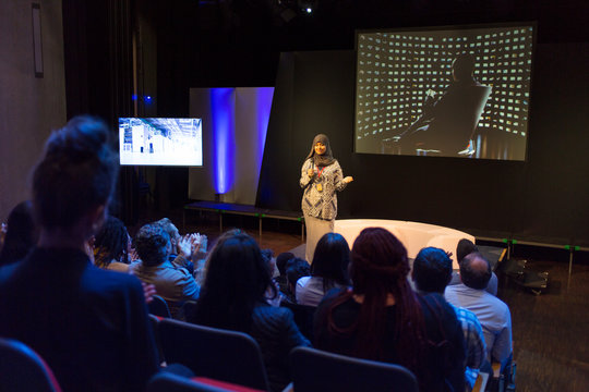 Female speaker in hijab on stage talking to conference audience
