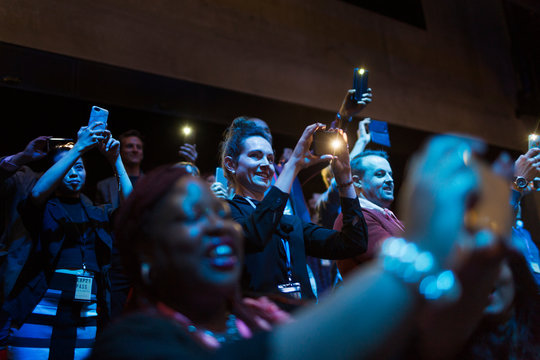 Smiling, Enthusiastic Audience Using Camera Phones In Dark Auditorium