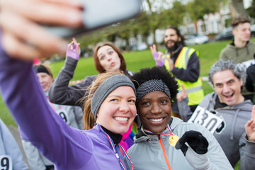 Smiling female runners with medal taking selfie at charity run in park