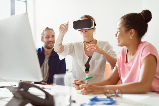 Computer programmers testing virtual reality simulator glasses at computer in office