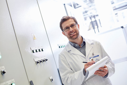 Portrait male technician in lab coat with clipboard in electrical control room