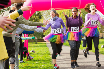 Spectators high-fiving female runners in tutus crossing charity run finish line