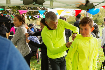Father pinning marathon bib on son at charity run in park tent