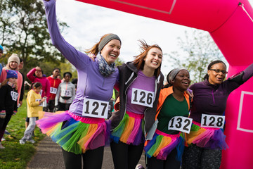 Enthusiastic female runners in tutus cheering, crossing finish line at charity run, celebrating