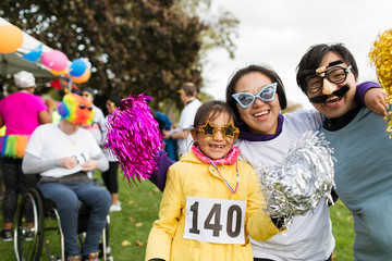 Portrait playful family wearing silly eyeglasses at charity run in park