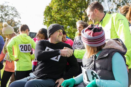 Runner shaking hands man in wheelchair at charity race in sunny park