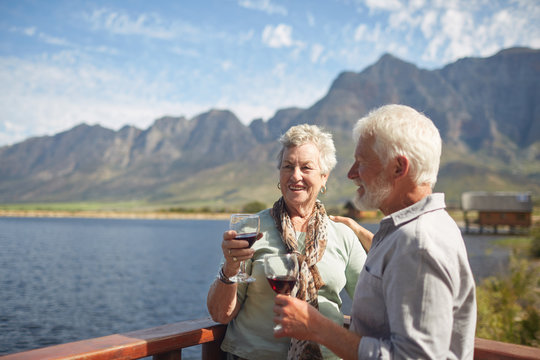 Smiling active senior couple drinking red wine on sunny summer lake balcony - Powered by Adobe