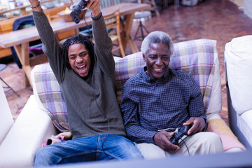 Enthusiastic grandfather and grandson playing video game on sofa