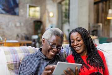Adult daughter teaching senior father how to use digital tablet on sofa