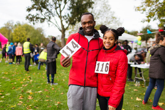 Portrait smiling, confident father daughter runners marathon bibs at charity run in park