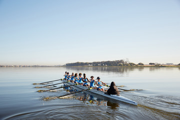 Female rowing team rowing scull on tranquil lake