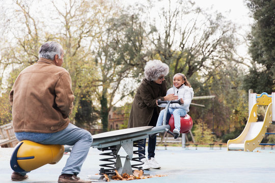 Grandparents playing with granddaughter on seesaw at playground