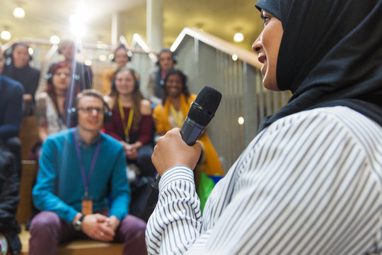 Smiling businesswoman in hijab speaking to audience with microphone