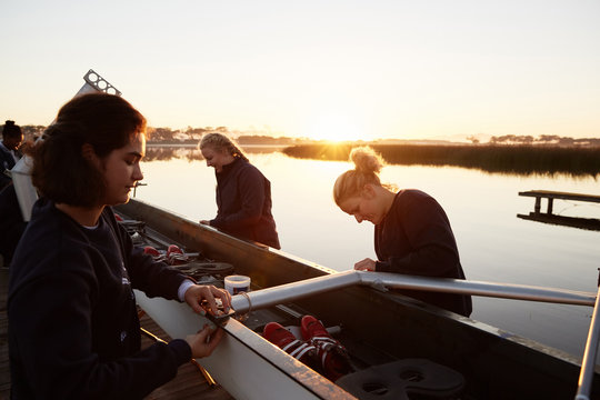 Female rowers preparing scull at sunrise lakeside