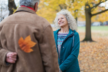 Playful senior husband surprising wife with autumn leaf in park