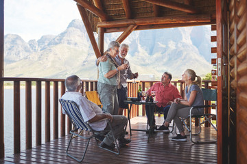 Active senior couple toasting friends wine glasses on lake cabin balcony