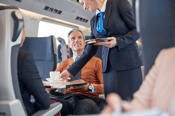 Attendant serving coffee to businessman on passenger train