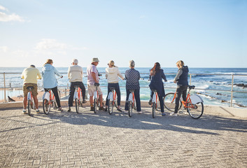 Active senior tourist friends on bicycles looking at sunny ocean view