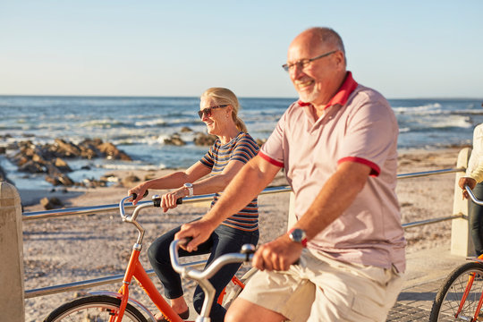 Smiling active senior tourists bike riding along sunny ocean - Powered by Adobe