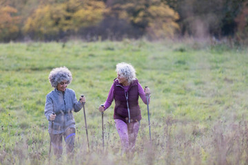 Active senior women friends hiking with poles up rural hillside