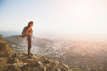 Female rock climber on top of hill overlooking sunny city