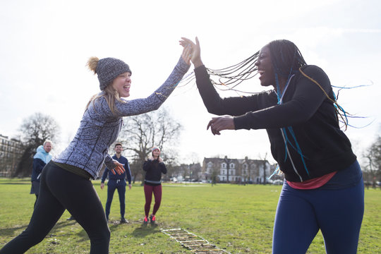 Enthusiastic women high-fiving, exercising in sunny park