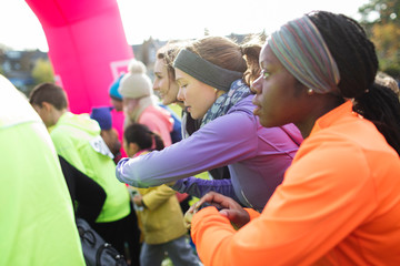 Focused female runners smart watches poised, ready at charity run starting line