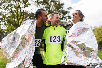 Happy male marathon runners wrapping in thermal blanket