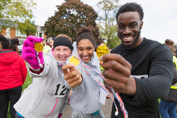Portrait enthusiastic runners showing medals at charity run in park