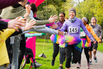 Enthusiastic female runners in tutus high-fiving spectators at charity run in park