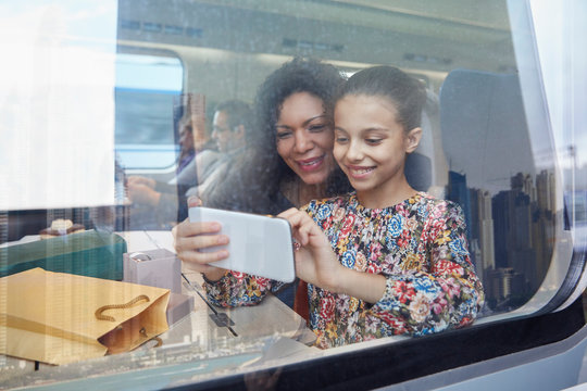 Mother and daughter using camera phone at window of passenger train