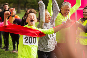 Enthusiastic boy runner crossing charity run finish line with family