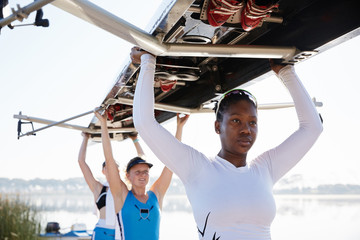 Confident, determined female rowing team lifting scull overhead
