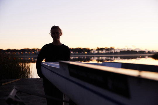 Silhouette of female rower lifting scull on sunrise lakeside dock